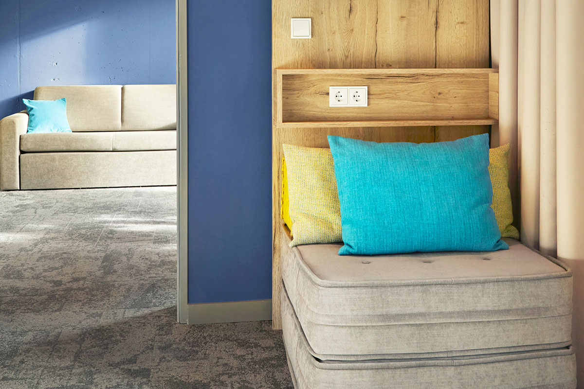 Ein Sessel und eine Couch als gemütliche Sitzmöglichkeiten mit bunten Kissen in der arborea Junior Suite im arborea Marina Resort Neustadt.