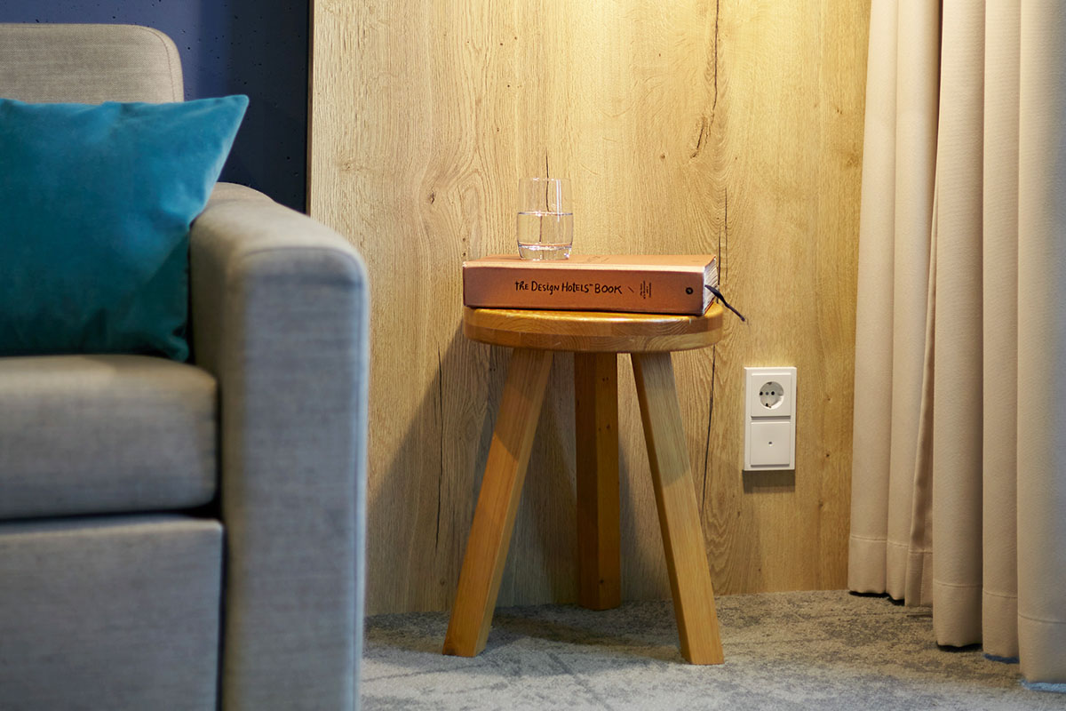 Kleiner Beistelltisch mit einem Buch und einem Glas Wasser neben der Couch in der arborea Junior Suite im arborea Marina Resort Neustadt.