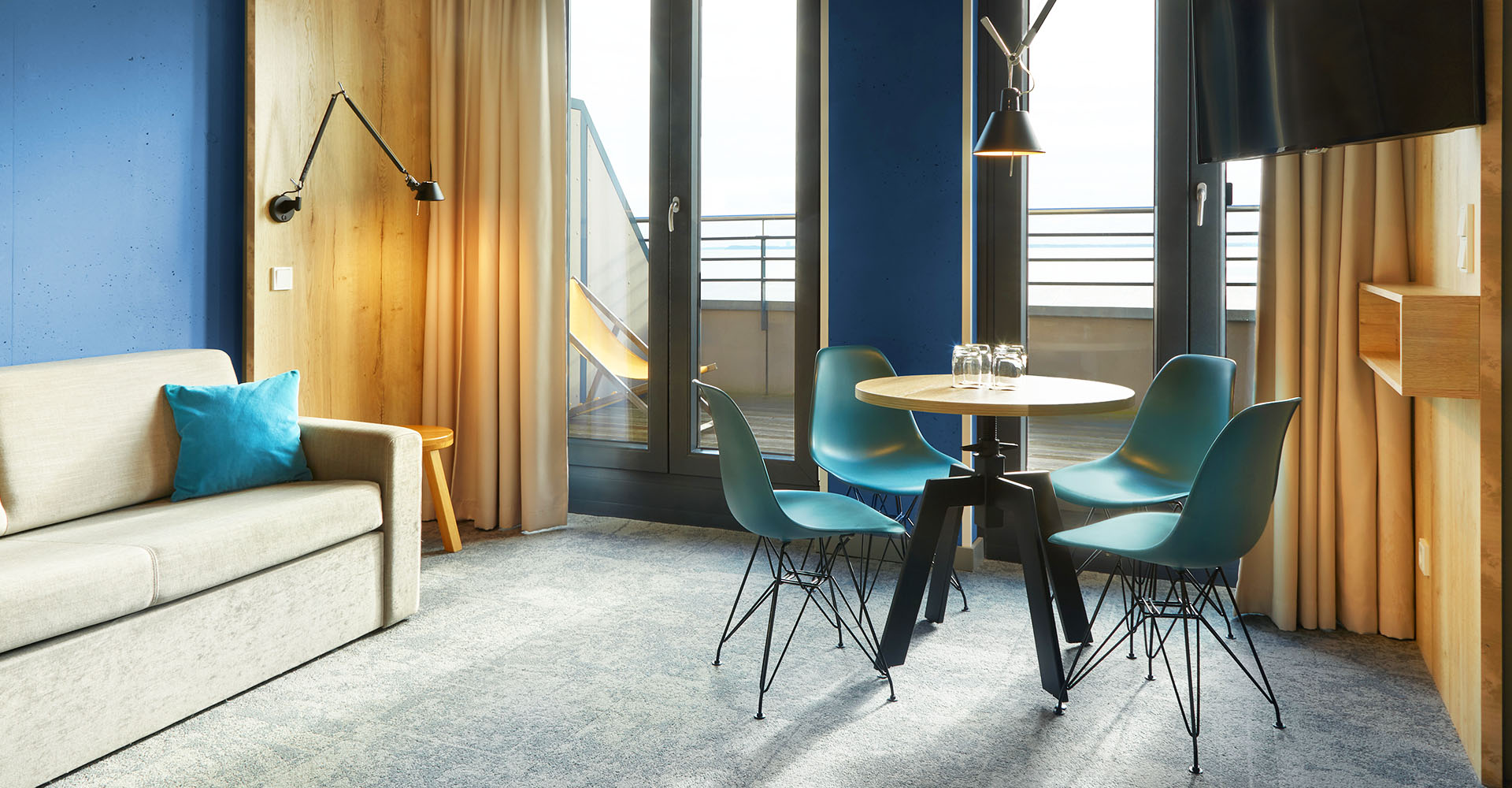 Der Wohnbereich mit Balkon, Couch, Esstisch mit Stühlen und TV in der arborea Junior Suite im arborea Marina Resort Neustadt.