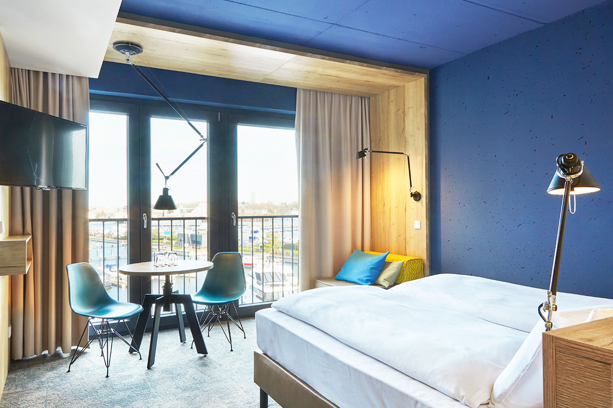 Kingsize Doppelbett, kleiner Esstisch mit Stühlen, TV und kleinem Sessel im Viererzimmer Auszeit im arborea Marina Resort Neustadt.